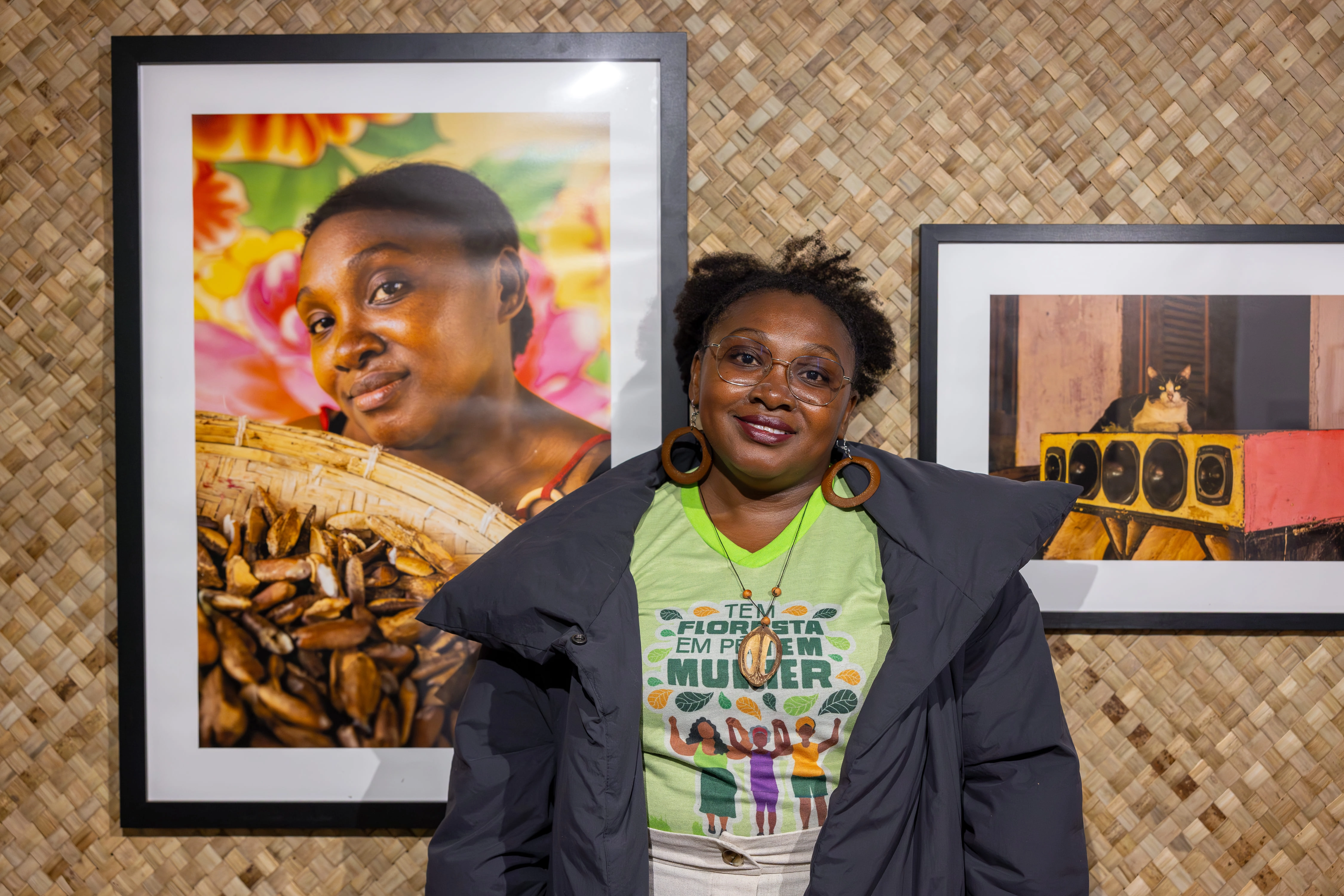 Foto mostra a quebradeira de coco babaçu Kleidianny Ferreira ao lado de seu retrato na exposição Women By Women, em Londres