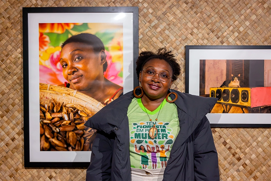 Foto mostra a quebradeira de coco babaçu Kleidianny Ferreira ao lado de seu retrato na exposição Women By Women, em Londres